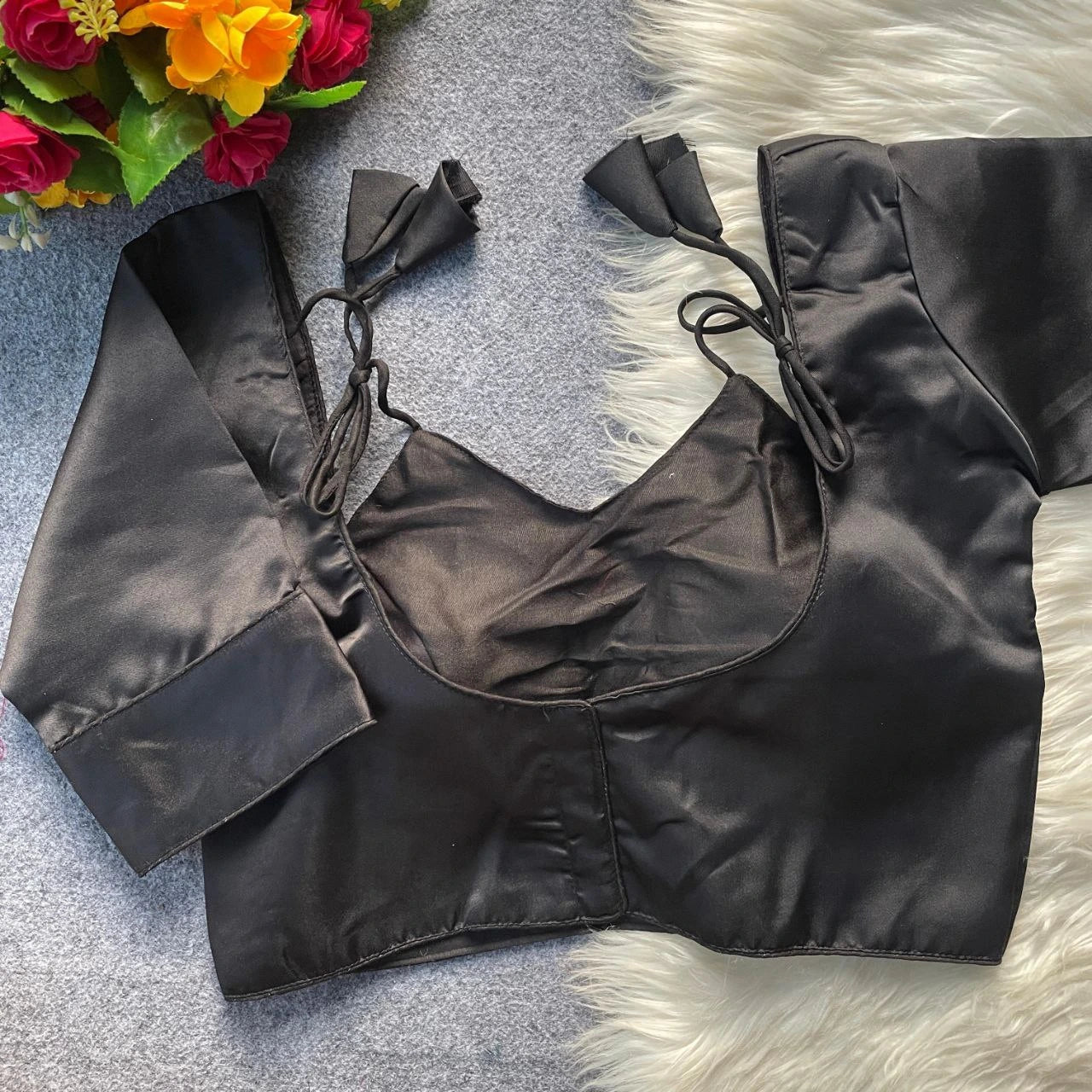 Black satin top on a textured surface with flowers in the corner